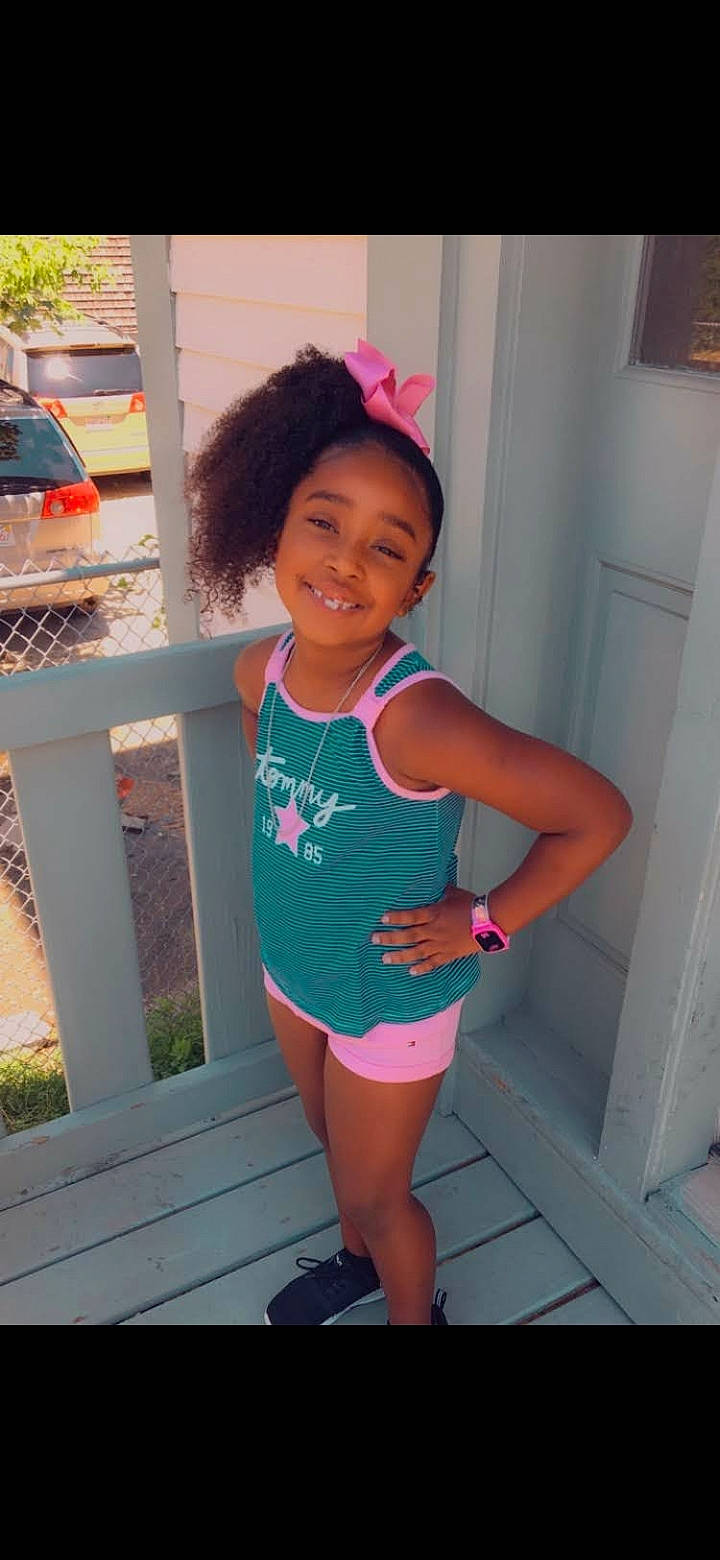 Londyn is registered to the contest to win money with this photo: black_hair, door, dress, electric_blue, face, happy, human_leg, joy, knee, leg, magenta, person, picture_frame, pink, plant, skin, smile, sportswear, thigh, toddler