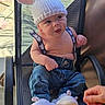 baby, child, knitted_hat, ears, denim_pants, suspenders, booties, mesh_chair, curious_expression, outdoor, sunlight, cute, infant, sitting, clothing, hand, footwear, person, portrait, playful