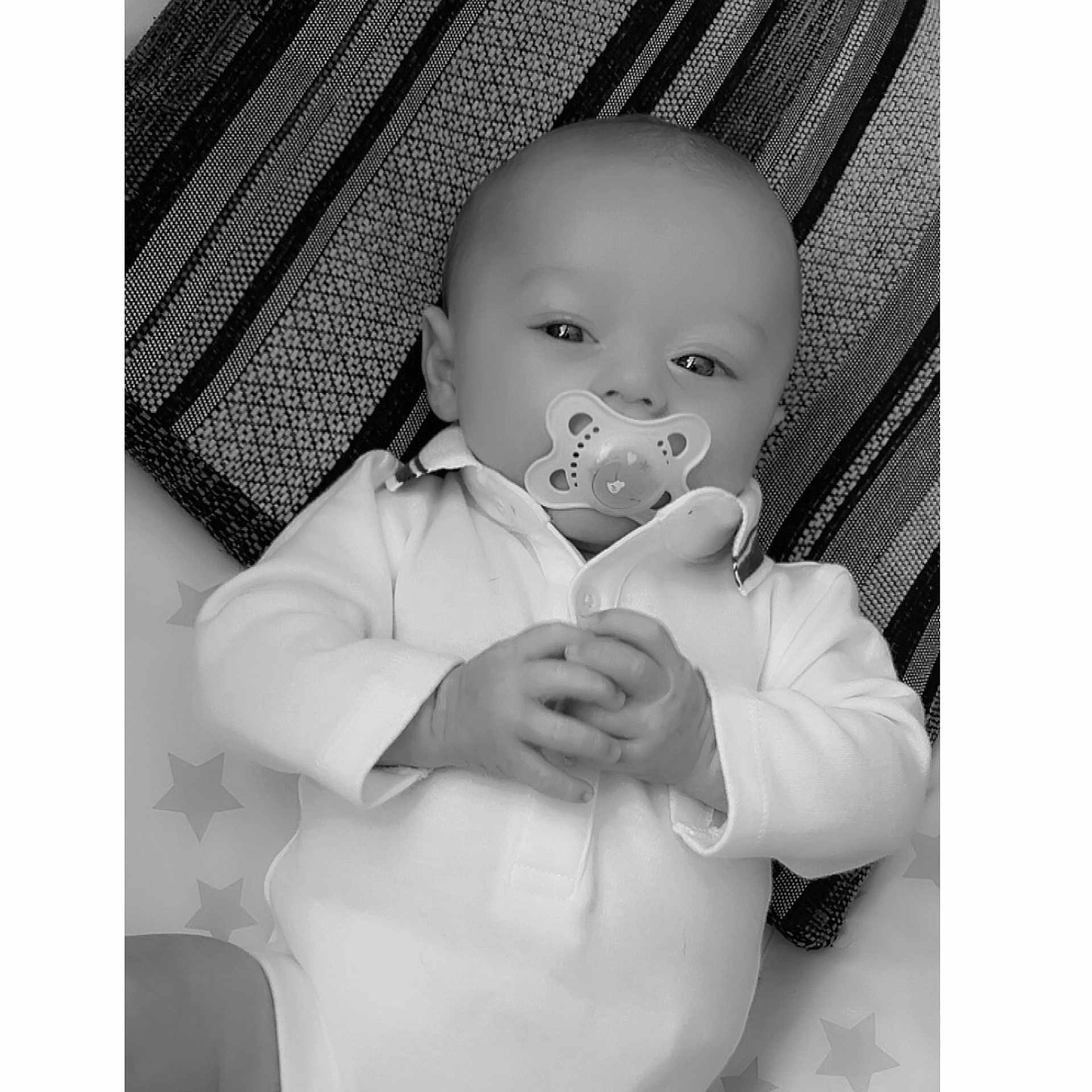 Kyron-James is registered to the contest to win money with this photo: baby, black_and_white, blanket, calm, child, clothing, cute, face, hands, infant, lying_down, monochrome, pacifier, pattern, portrait, resting, stars, striped_background, white_outfit, young_baby