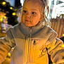 Giulia a rejoint le concours — aidez-le/la à gagner de superbes lots ! child, toddler, jacket, zipper, fleece, pony_tail, blonde_hair, face, eyes, cheeks, portrait, bokeh, holiday_lights, night, festive, warm_tones, outdoor, blurred_background, cute, curious