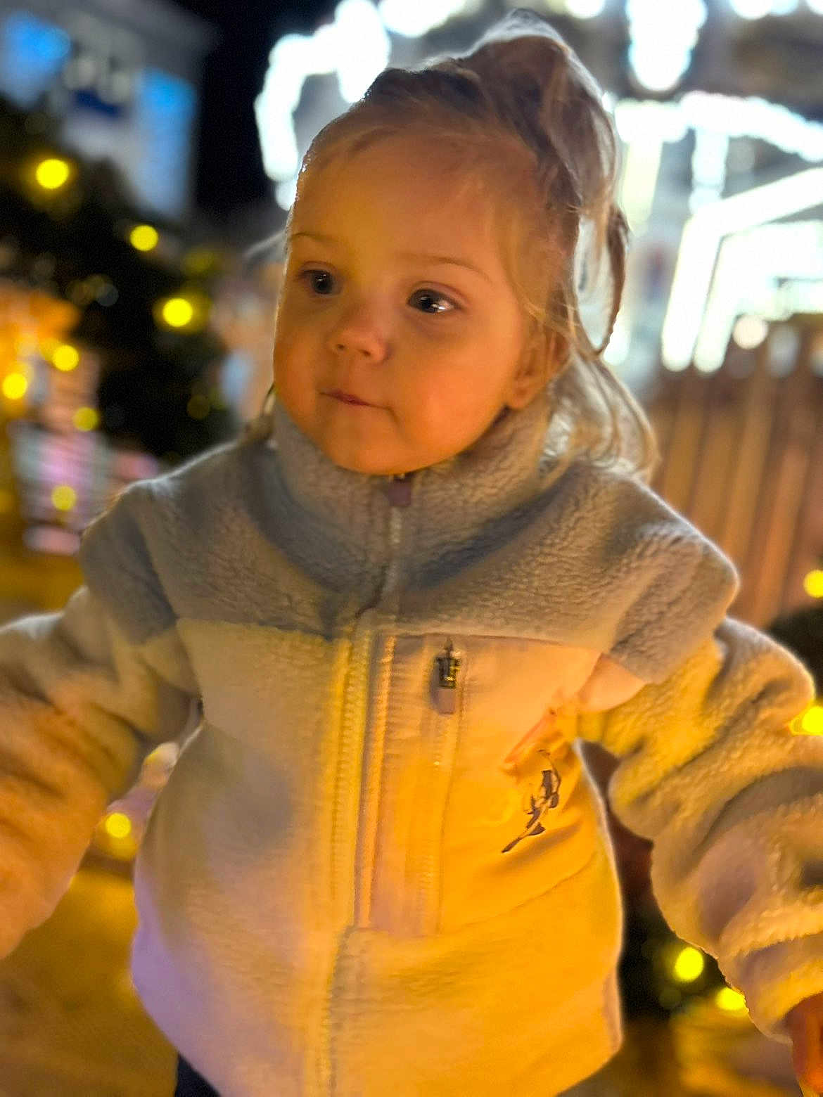Giulia a rejoint le concours — aidez-le/la à gagner de superbes lots ! child, toddler, jacket, zipper, fleece, pony_tail, blonde_hair, face, eyes, cheeks, portrait, bokeh, holiday_lights, night, festive, warm_tones, outdoor, blurred_background, cute, curious