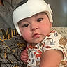 baby, infant, child, helmet, protective_gear, onesie, animal_print, person, face, eyes, cheeks, hand, shirt, gray_clothing, indoor, couch, upclose, curious, portrait, holding