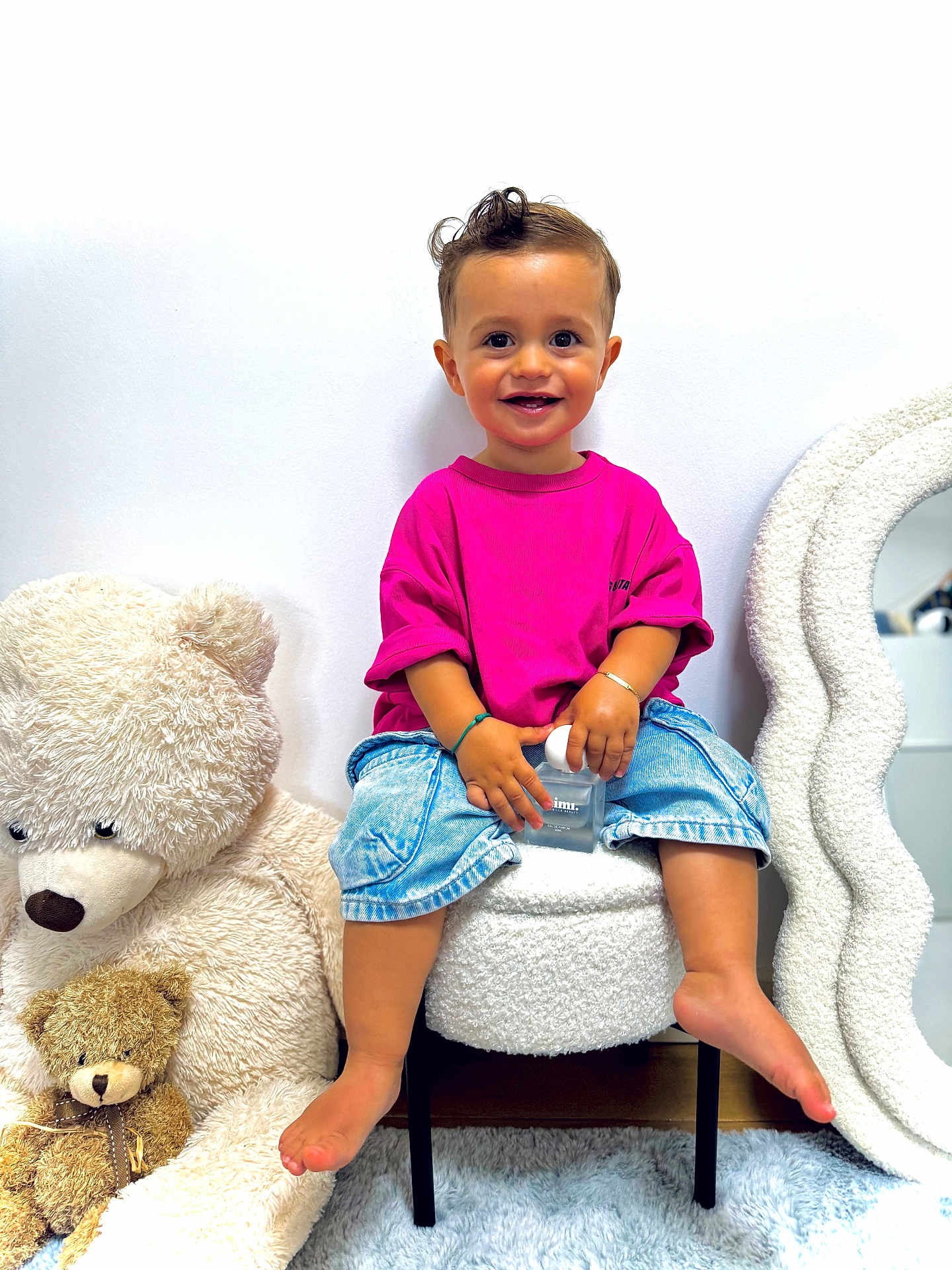 Milann a rejoint le concours — aidez-le/la à gagner de superbes lots ! toddler, child, smiling, pink_shirt, denim_shorts, barefoot, stuffed_teddy_bear, plush_toy, white_wall, mirror, chair, carpet, indoor, cute, happy, portrait, sitting, toy, cozy, home_decor