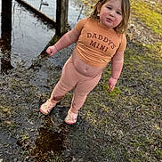 Leila is registered to the contest to win money with this photo: toddler, child, muddy, puddle, outdoor, grass, shirt, clothing, shoes, mud, face, person, standing, nature, playful, messy, casual, expression, daylight, young