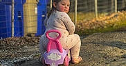 Leila is registered to the contest to win money with this photo: bins, blue, casual, child, curious, daylight, dirt_path, face, fence, looking_back, outdoor, pajamas, person, pink, playful, purple, ride_on_toy, toddler, toy, yellow