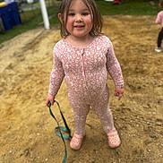 Leila is registered to the contest to win money with this photo: background, casual_clothing, child, crocs, daylight, footwear, fun, grass, happy, leash, long_hair, nature, outdoor, person, pink_onesie, play, playground, sand, smiling, toddler