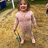 background, casual_clothing, child, crocs, daylight, footwear, fun, grass, happy, leash, long_hair, nature, outdoor, person, pink_onesie, play, playground, sand, smiling, toddler
