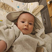 Alban participe au concours pour gagner de l'argent avec cette photo : baby, child, towel, hooded_towel, bunny_ears, face, infant, cute, soft_texture, kitchen, cabinet, wooden_counter, baby_mat, colorful, portrait, indoor, skin, expression, eyes, person