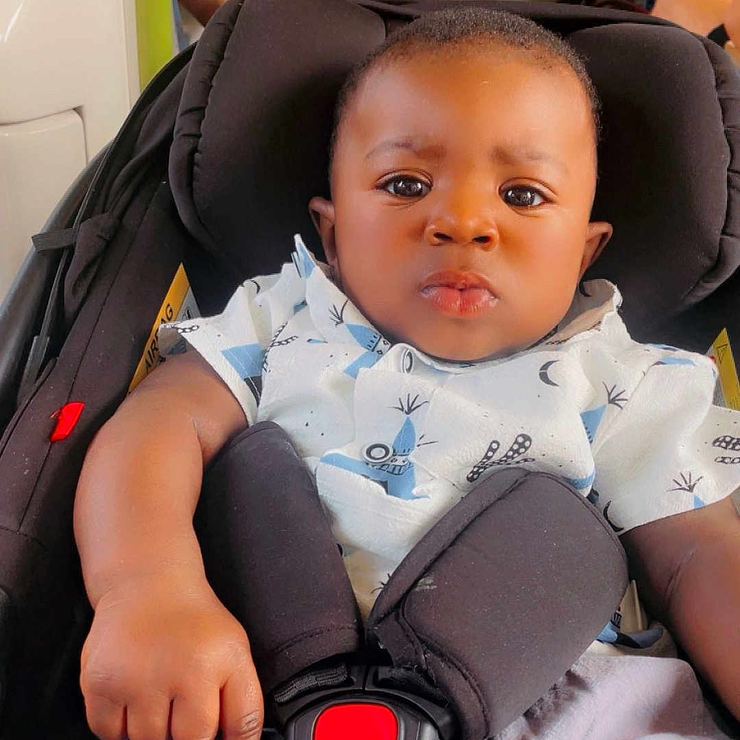 Liam a rejoint le concours — aidez-le/la à gagner de superbes lots ! baby, black_hair, bus, car_seat, child, clothing, expression, hand, indoor, infant, people, person, public_transport, seatbelt, serious, shirt, shorts, shoulder, sitting, skin