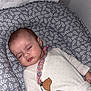baby, sleeping, onesie, blanket, pacifier_clip, cushion, floral_pattern, infant, child, resting, indoors, peaceful, cute, soft_texture, head, face, hand, nap, comfort, cozy
