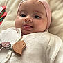 baby, infant, face, tongue, pink_hat, white_sweater, knitted_clothing, lying_down, soft_blanket, toy, colorful, cute, child, playful, closeup, indoors, skin, happy, smiling, person