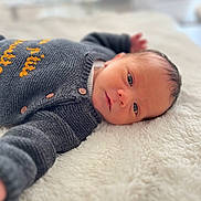 Gabriel a rejoint le concours — aidez-le/la à gagner de superbes lots ! baby, infant, newborn, lying_down, blanket, knitted_sweater, gray_clothing, face, eyes, cozy, soft_texture, indoor, portrait, cute, young_child, child, warm, sleepy, resting, human