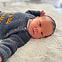 baby, infant, newborn, lying_down, blanket, knitted_sweater, gray_clothing, face, eyes, cozy, soft_texture, indoor, portrait, cute, young_child, child, warm, sleepy, resting, human