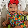 baby, child, smiling, headband, red_bow, fruit_pattern, colorful_clothing, toy, insect_toy, seat, cushion, happy, infant, cute, portrait, indoors, playful, holding, skin, arm