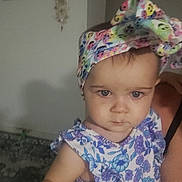 Kelsey joined the competition — help win amazing prizes! baby, child, headband, floral_dress, blue_eyes, person, indoor, wall_clock, decor, holding, arm, cute, serious, portrait, infant, clothing, headwear, human, face, skin