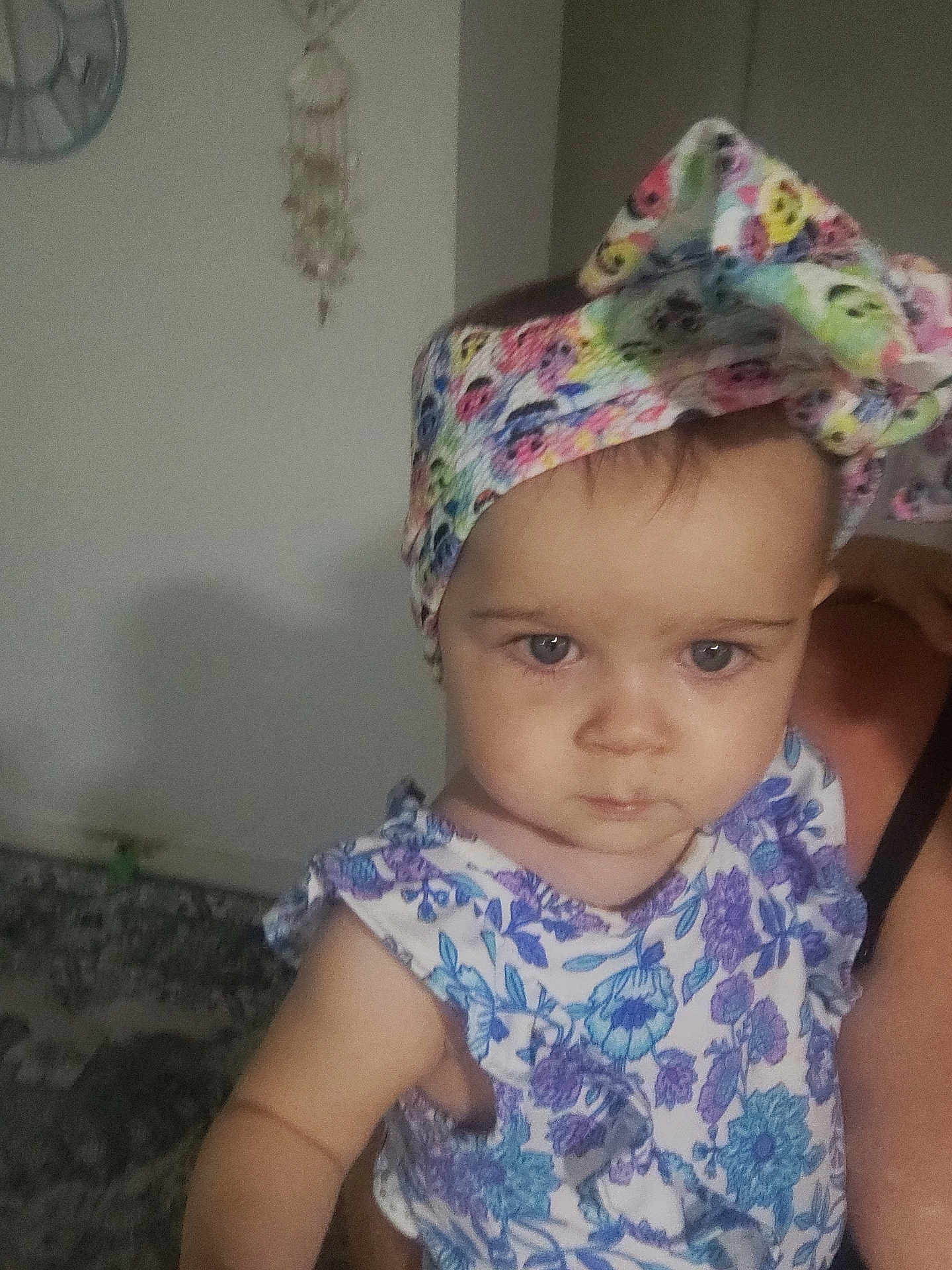 Kelsey joined the competition — help win amazing prizes! baby, child, headband, floral_dress, blue_eyes, person, indoor, wall_clock, decor, holding, arm, cute, serious, portrait, infant, clothing, headwear, human, face, skin