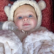 Léna a rejoint le concours — aidez-le/la à gagner de superbes lots ! baby, blanket, blue_eyes, bottle, child, cozy, cute, expression, face, fluffy_clothing, headgear, hood, indoor, infant, onesie, pink_background, portrait, smile, soft_texture, warm_clothing