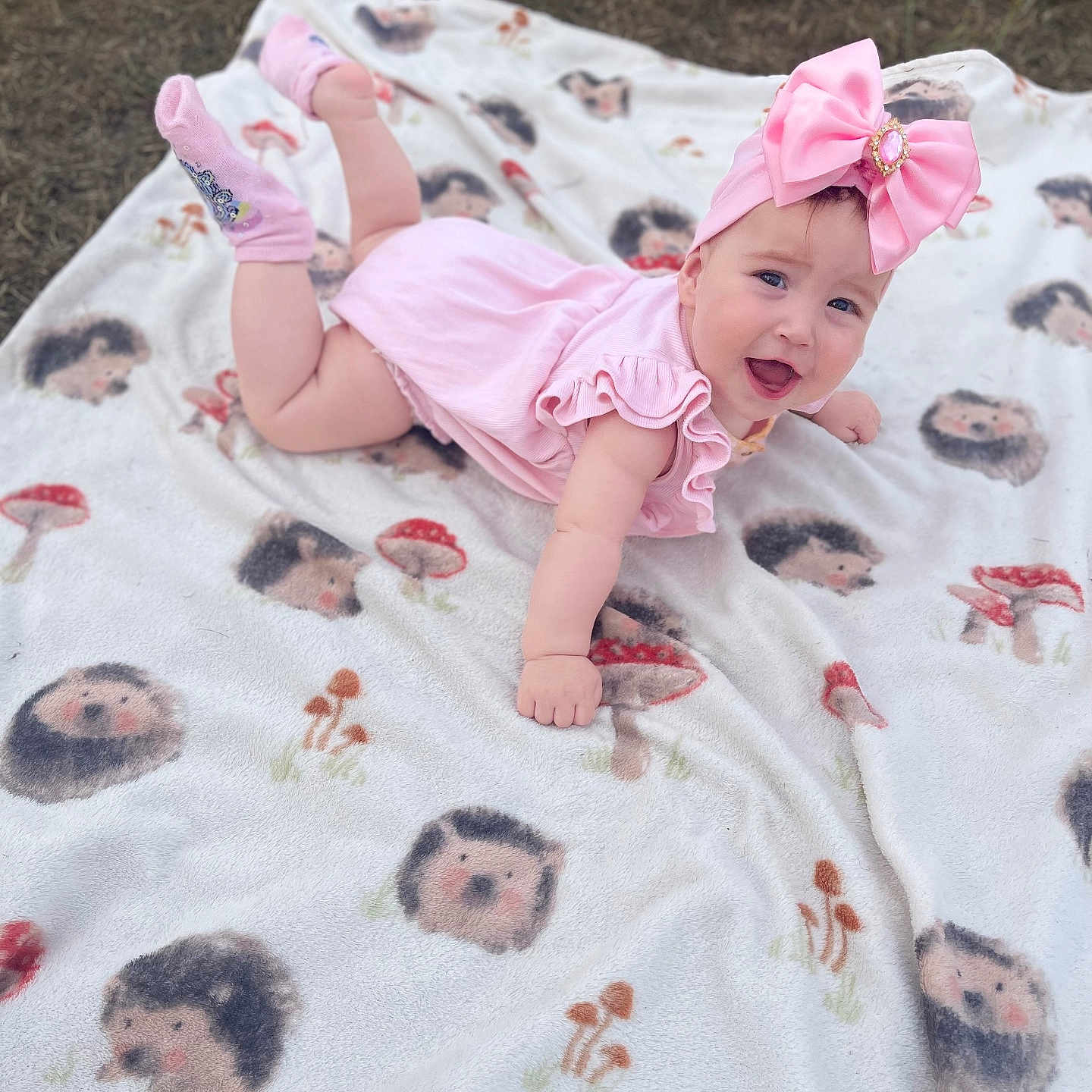 Erika is registered to the contest to win money with this photo: baby, blanket, bow, child, clothing, cute, grass, happy, headband, hedgehog_pattern, infant, mushroom_pattern, outdoor, pink_dress, playtime, portrait, smiling, sock, soft_texture, tummy_pose