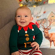 Myles is registered to the contest to win money with this photo: baby, child, smiling, holiday, christmas, pajamas, striped_pants, couch, pillow, reindeer, decor, indoor, portrait, cute, festive, happy, infant, person, seated, cozy