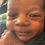 Josiah is registered to the contest to win money with this photo: baby, closeup, face, hand, smile, child, skin, expression, eyes, cute, infant, portrait, young, person, resting, indoors, natural_light, warm, soft, charming