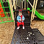 toddler, child, playground, playground_equipment, slide, steps, woodchips, pacifier, denim_jacket, red_clothing, bow, outdoor, person, green, orange, black, curious, sitting, baby_shoes, daylight