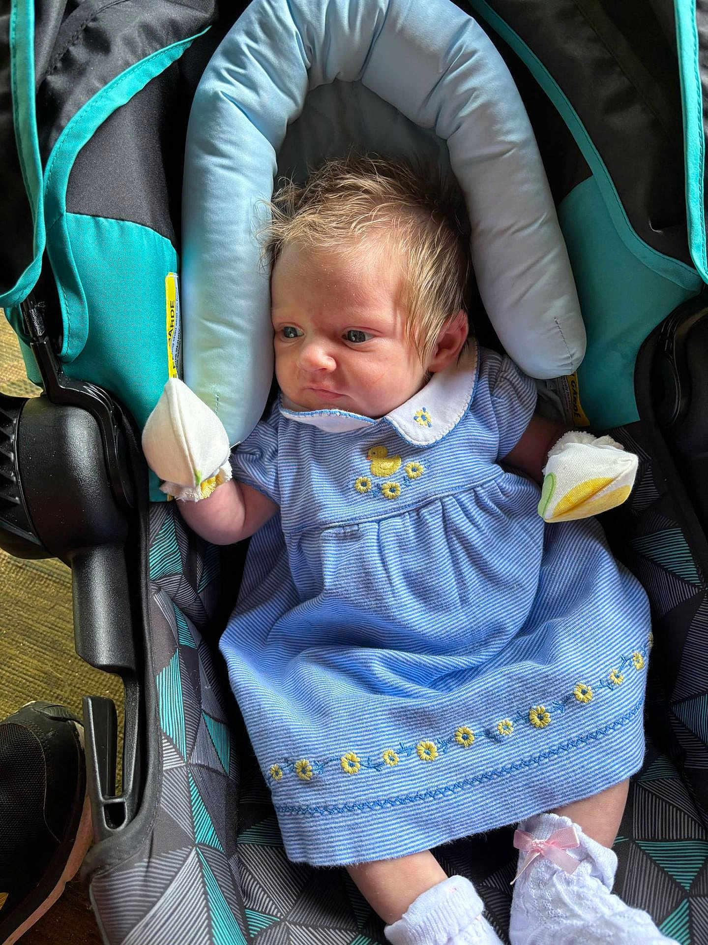 Gabriella joined the competition — help win amazing prizes! baby, infant, car_seat, blue_dress, mittens, socks, face, person, child, cute, newborn, clothing, pattern, fabric, seat, indoor, portrait, expression, hair, footwear
