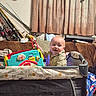 Dakota is registered to the contest to win money with this photo: baby, child, playpen, toy, fishing_rods, couch, curtains, plaid_shirt, indoors, smile, happy, person, play, colorful, furniture, blanket, head, face, living_room, home