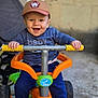 baby, child, smiling, cap, blue_shirt, tricycle, toy, outdoor, happy, hands, face, person, footwear, pants, play, ride, vehicle, colorful, young, expression