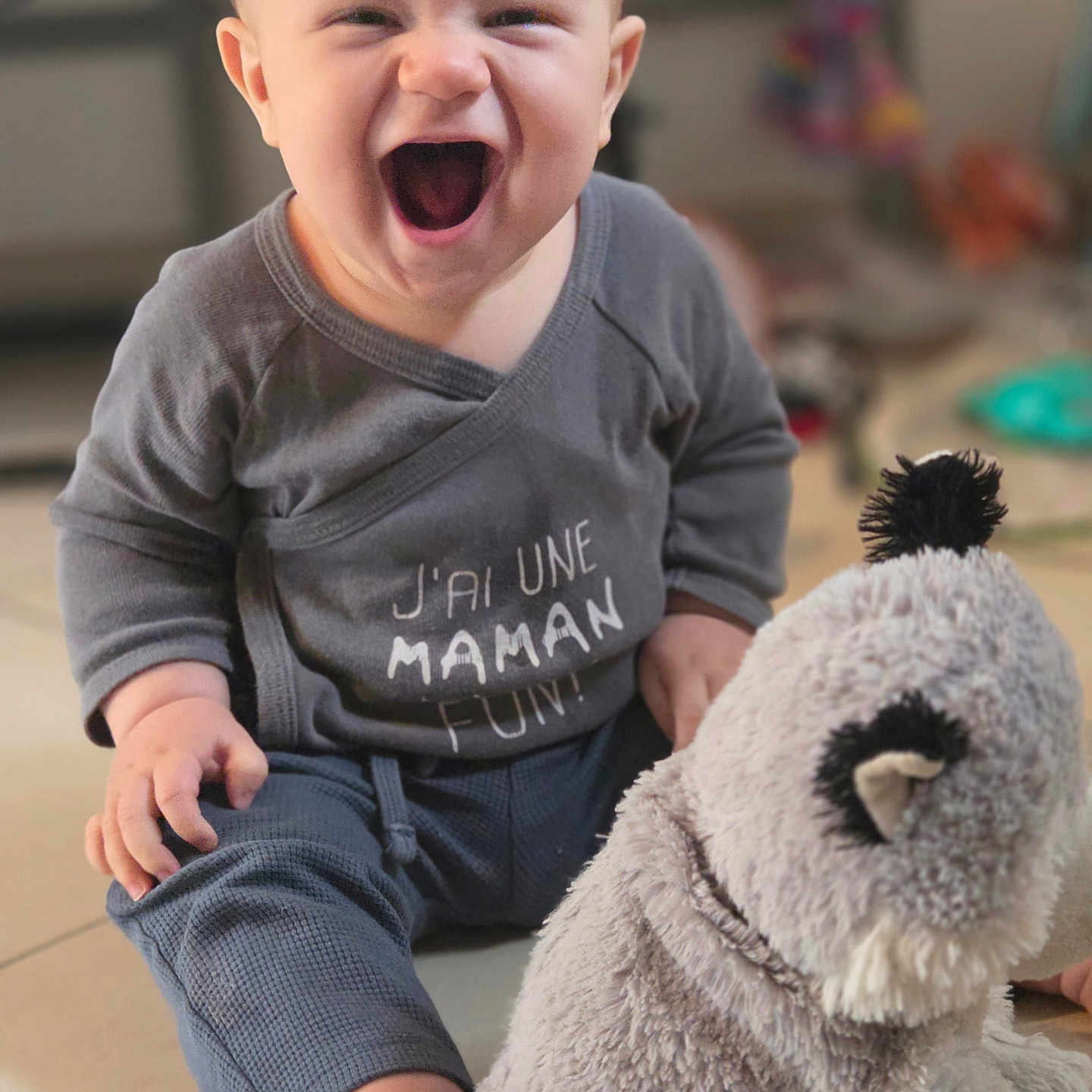 Lyam participe au concours pour gagner de l'argent avec cette photo : baby, blurred_background, child, clothing, cute, face, floor, grey_clothing, happy, indoor, infant, mouth_open, person, playful, sitting, smiling, soft_toy, stuffed_animal, toy, young_child