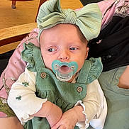 Lillyann joined the competition — help win amazing prizes! baby, infant, pacifier, headband, bow, green_dress, corduroy, button, hands, adult_hand, car_seat, blanket, pink_pattern, wooden_floor, table, chair_leg, jacket, portrait, side_glance, indoor