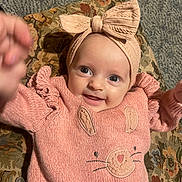 Lillyann joined the competition — help win amazing prizes! baby, bow, child, closeup, cushion, cute, face, hands, happy, headband, indoor, infant, knitted_clothing, patterned_fabric, person, pink_sweater, playful, portrait, reaching, smiling