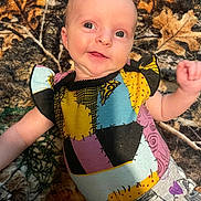 Lillyann is registered to the contest to win money with this photo: baby, infant, smile, lying_down, blanket, leaf_pattern, colorful_clothing, patchwork, portrait, face, eyes, cheeks, arm, hand, newborn, cozy, fabric, home_interior, cute, playful