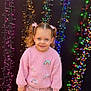 child, girl, smiling, pink_sweater, rainbow, curly_hair, pigtails, fairy_lights, colorful_lights, background, outdoor, casual_clothing, pants, sneakers, happy, portrait, standing, cute, blue_eyes, festive