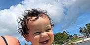 Sofia is registered to the contest to win money with this photo: toddler, child, smiling, curly_hair, swimsuit, colorful_clothing, beach, water, ocean, sky, clouds, sunny, outdoor, person, holding, vacation, summer, nature, happy, portrait