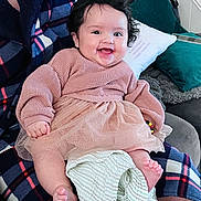 Maeve is registered to the contest to win money with this photo: baby, blanket, child, clothing, couch, cozy, cute, fabric, face, foot, hair, hand, happy, indoors, infant, person, pillow, sitting, smile, textile