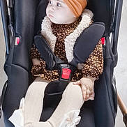 Janna participe au concours pour gagner de l'argent avec cette photo : baby, infant, car_seat, stroller, headband, bow, face, seat_belt, buckle, tights, patterned_clothing, fur_trim, hand, wheel, pensive_expression, cute, portrait, indoors, footwear_bow, child