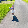 bonnet, car, child, cute, daylight, doll, grass, greenery, happy, nature, outdoor, pavement, person, road, shadow, suburban, sunlight, toy, walking, white_dress