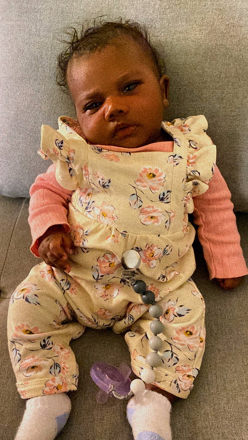 Noelle is registered to the contest to win money with this photo: baby, baby_toddler_clothing, camouflage, cheek, child, collar, comfort, gesture, leg, military_camouflage, nightwear, nose, outerwear, pattern, person, pink, sitting, skin, sleeve, textile