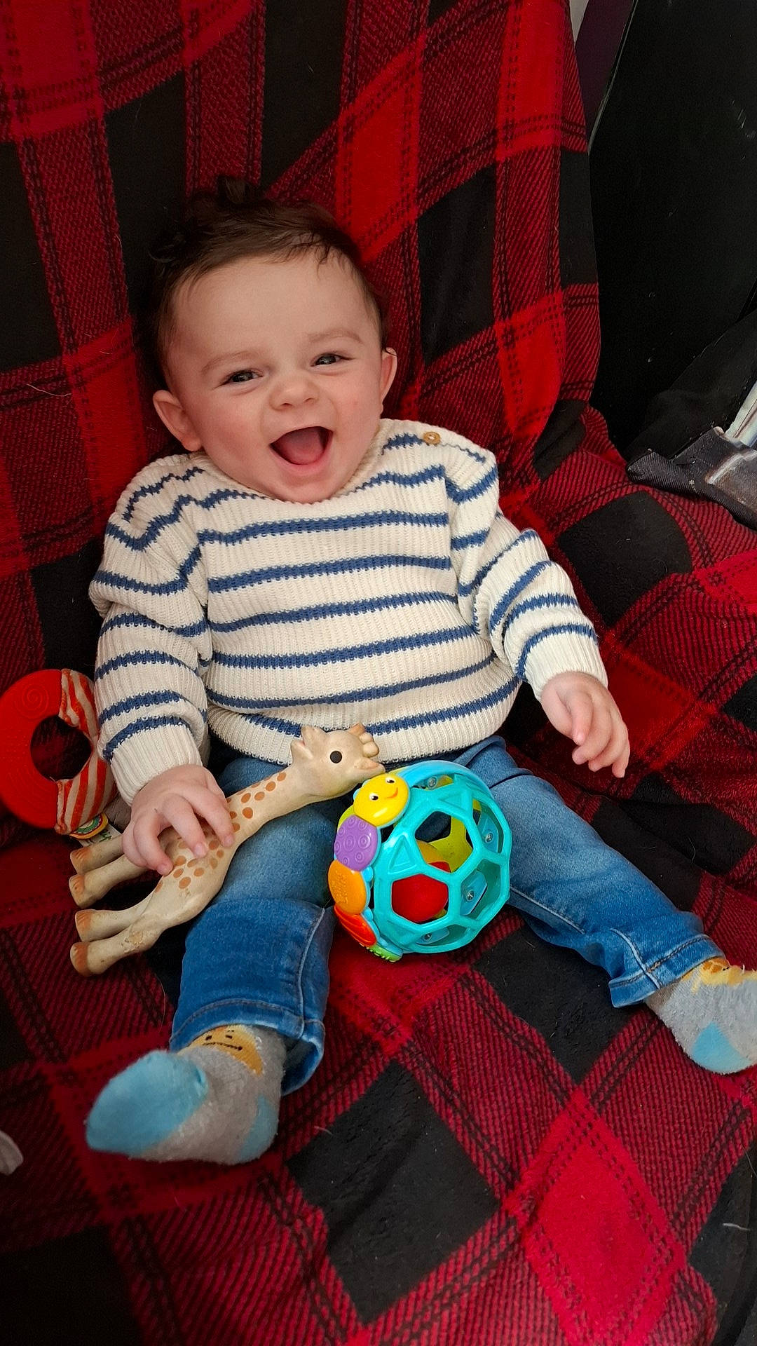 Gabriel participe au concours pour gagner de l'argent avec cette photo : arm, baby_playing_with_toys, baby_toddler_clothing, cheek, comfort, couch, eye, finger, fun, happy, head, leg, person, plaid, red, sleeve, smile, tartan, textile, toddler