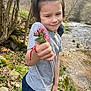 Erik is registered to the contest to win money with this photo: child, flower, outdoor, river, nature, smile, trees, rocks, grass, creek, shirt, pants, bracelet, hand, person, spring, daylight, casual_clothing, gift, forest