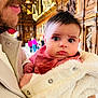 baby, child, person, adult, face, mustache, jacket, bib, hand, indoor, wood_paneling, ornate, blurred_background, curious, wide_eyes, cozy, holding, portrait, expression, warm_clothing