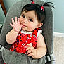 Adelaide is registered to the contest to win money with this photo: baby, child, pigtails, ladybug_clips, red_dress, floral_pattern, smiling, cute, seated, gray_seat, car_seat, indoor, carpet, wall, hand, face, person, young_child, happy, playful
