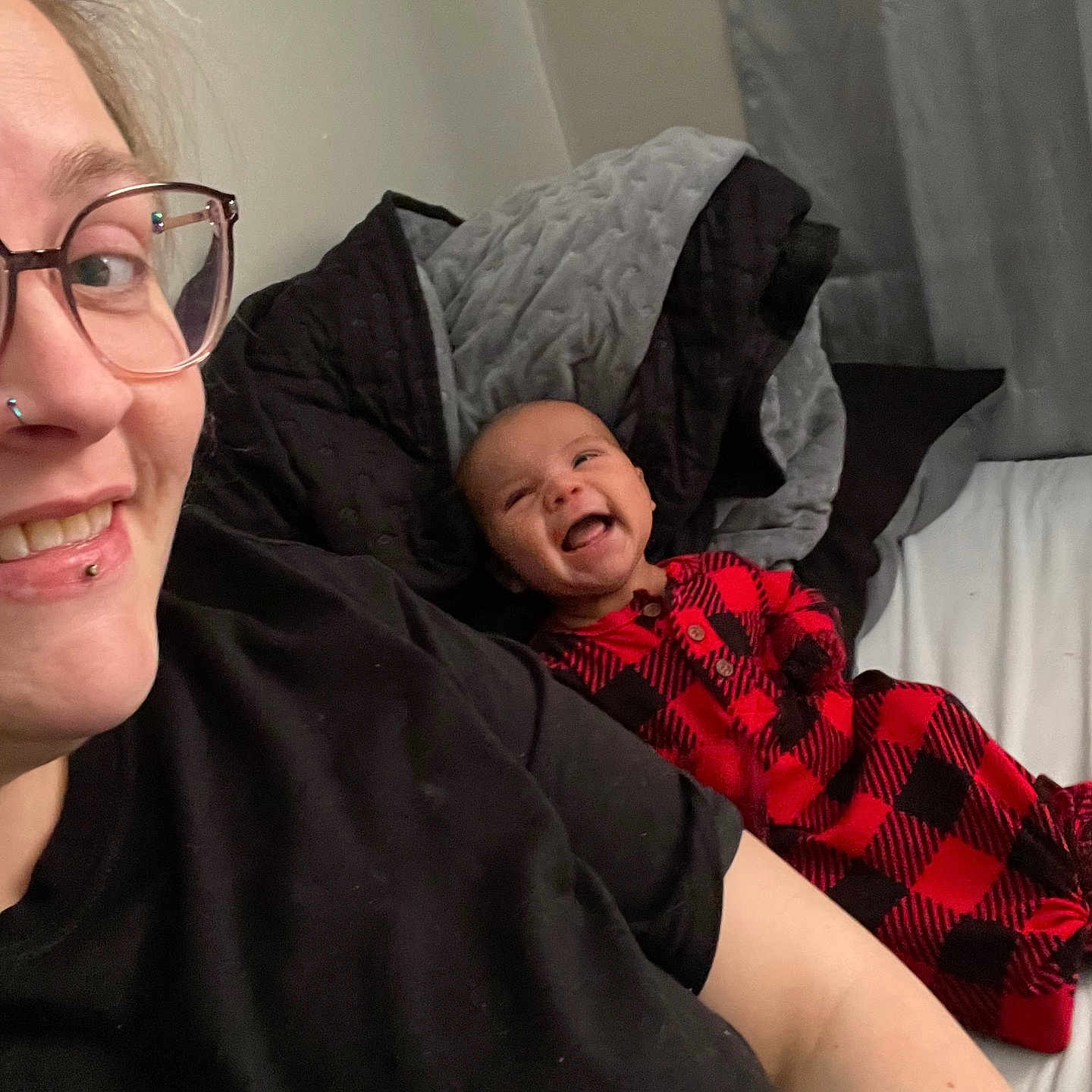 Zayden is registered to the contest to win money with this photo: adult, baby, bed, black_clothing, blanket, checkered_pattern, curtain, eyewear, facial_piercing, glasses, happy, indoor, laughing, person, plaid, portrait, smile, tattoo, toddler, wearing