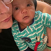 Zayden joined the competition — help win amazing prizes! baby, adult, glasses, piercing, onesie, striped_clothing, hand, indoor, face, closeup, expression, curious, holding, person, fabric, blue, red_clip, comfort, skin, couch
