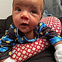 Zayden is registered to the contest to win money with this photo: baby, infant, pajamas, mittens, cushion, pattern, red, white, blue, yellow, face, eyes, expression, toddler, child, indoor, closeup, person, cute, curious