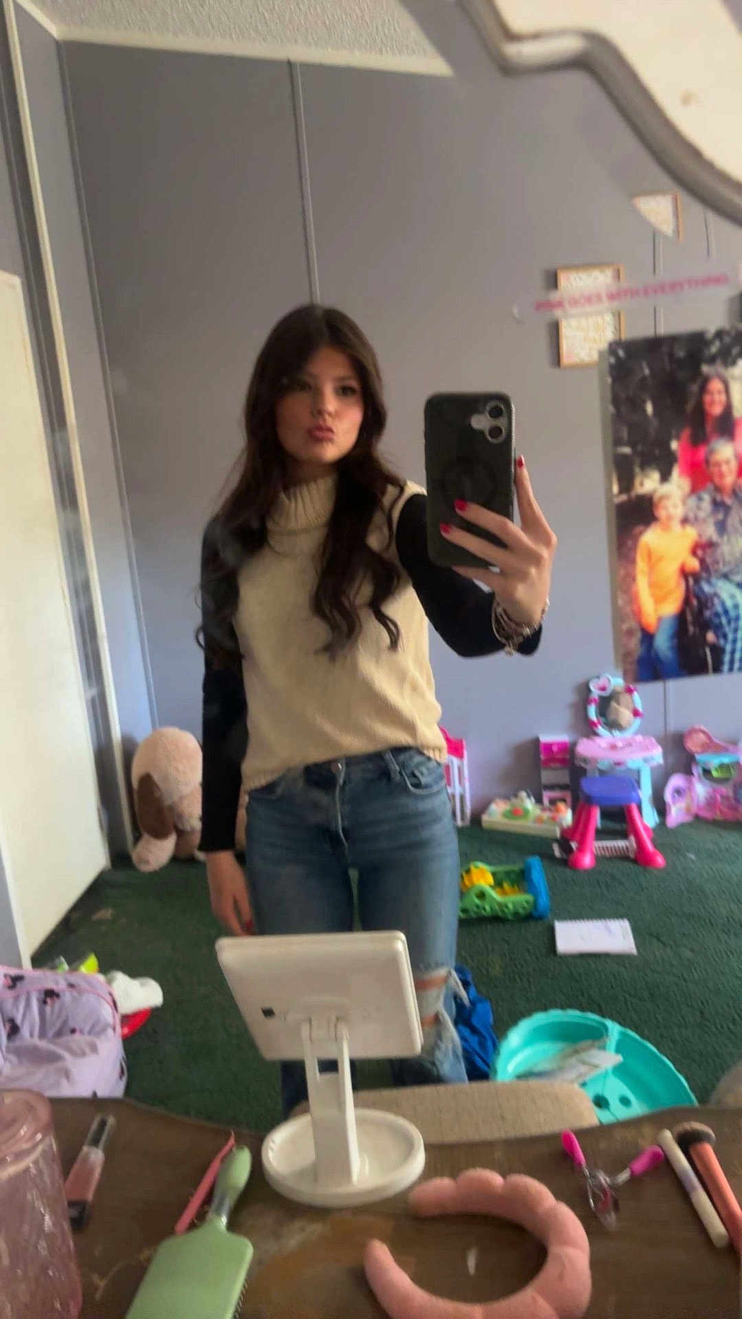 Brinley is registered to the contest to win money with this photo: person, mirror, selfie, jeans, long_hair, sweater, room, toys, mirror_selfie, smartphone, casual_clothing, carpet, makeup_brush, hairbrush, table, child_toys, poster, pink, green, reflection