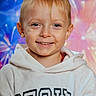 blonde_hair, blue_eyes, casual_clothing, child, colorful_background, cute, face, fireworks_effect, happy, head_and_shoulders, hoodie, indoor, kid, light_skin, person, photography, portrait, smiling, studio_background, young_child