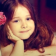 Alice a rejoint le concours — aidez-le/la à gagner de superbes lots ! child, girl, portrait, smiling, long_hair, flower_accessory, hair, face, eyes, lying_down, hand_on_face, indoor, soft_lighting, close_up, rosy_cheeks, pink_flower, bed, hair_accessory, relaxed, young_child