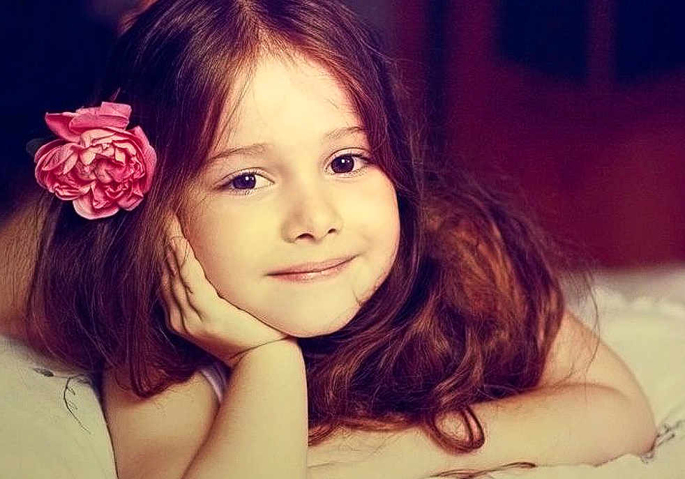 Alice a rejoint le concours — aidez-le/la à gagner de superbes lots ! child, girl, portrait, smiling, long_hair, flower_accessory, hair, face, eyes, lying_down, hand_on_face, indoor, soft_lighting, close_up, rosy_cheeks, pink_flower, bed, hair_accessory, relaxed, young_child