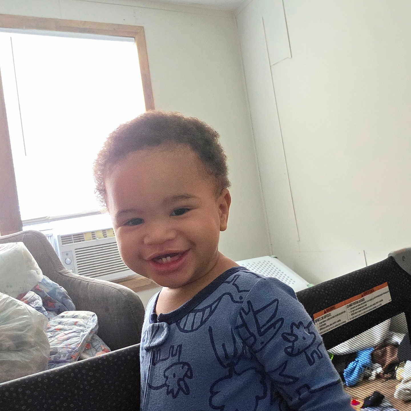 Jayden joined the competition — help win amazing prizes! toddler, child, smiling, indoor, onesie, dinosaur_pattern, baby, face, air_conditioner, chair, window, toys, floor, happy, home, person, clothing, portrait, furniture, playpen